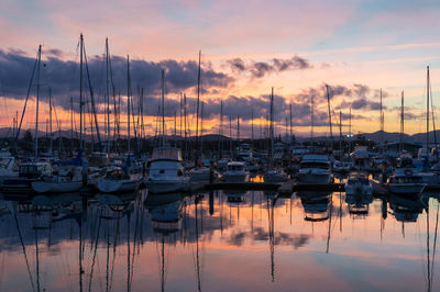 Boats moored in harbor at sunset