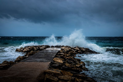 Waves splashing on rocks at shore against sky