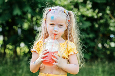 Outdoor portrait of funny grimy little girl with two ponytails drinks lemonade sweet sweetened