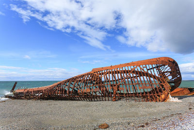 Abandoned metallic structure on beach against sky