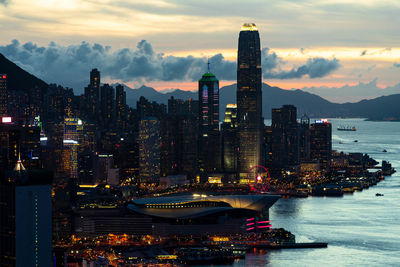 Illuminated city by sea against sky at night