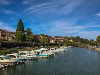 Sailboats moored on river by buildings against blue sky