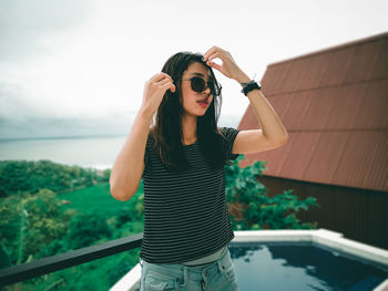 Young woman wearing sunglasses standing against sky