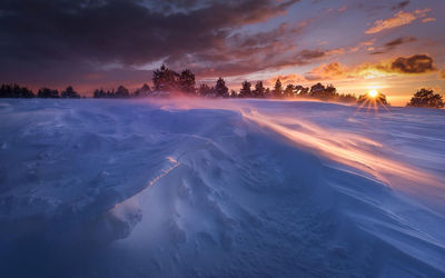 Scenic view of snow covered field against cloudy sky during sunset