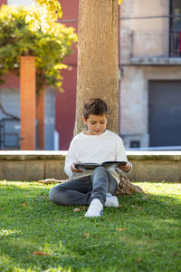 Little kid reading a book in a shade of a tree