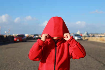 Shy boy covering face with hood while standing on road