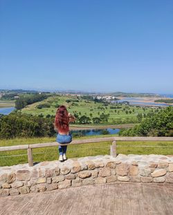 Rear view of woman sitting on railing against clear sky