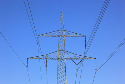 Low angle view of electricity pylon against clear blue sky