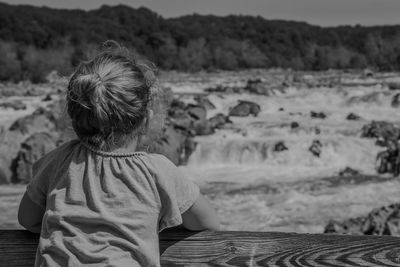 Rear view of girl leaning on fence looking at flowing stream