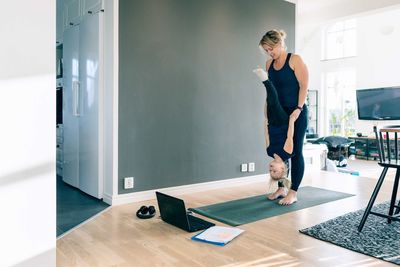 Mother holding daughter upside down while standing on mat in living room