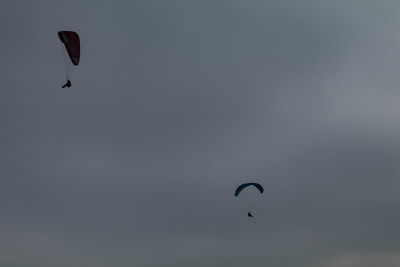 Low angle view of people paragliding against sky