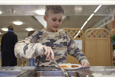 Schoolboy putting food on plate in cafeteria