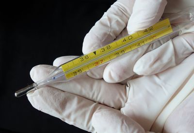 Hands in medical or surgical glove holding a mercury thermometer