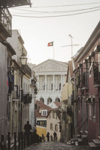 People walking on street amidst buildings in city against sky