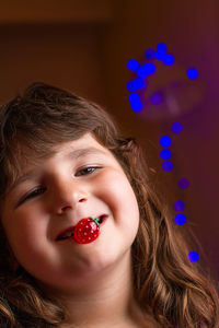 Close-up portrait of smiling girl with toy strawberry in her mouth