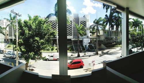 Trees and cars in city against sky seen through window