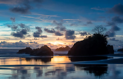 Silhouette rocks by sea against sky during sunset