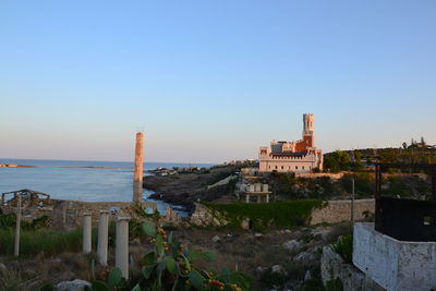 Buildings by sea against clear blue sky