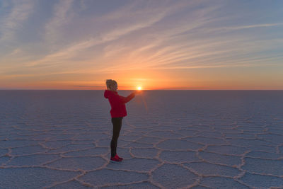 Woman standing on salt flat against sky during sunset