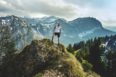 Portrait of mature man standing on mountain peak against cloudy sky