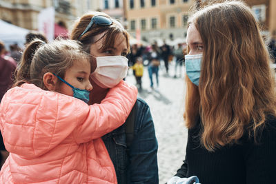 Family mother and her daughters standing in a street downtown wearing the face masks to avoid virus