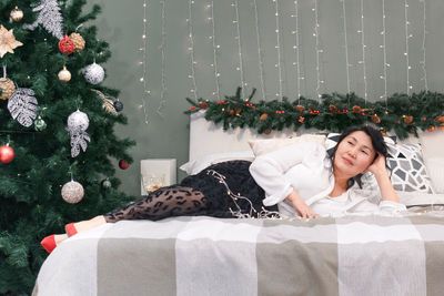 Senior asian woman rest on bed with xmas decoration and lights, elderly lady relax at christmas home