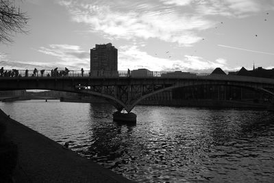 Bridge over river by buildings against sky