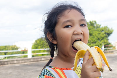 Portrait of cute girl eating banana on road