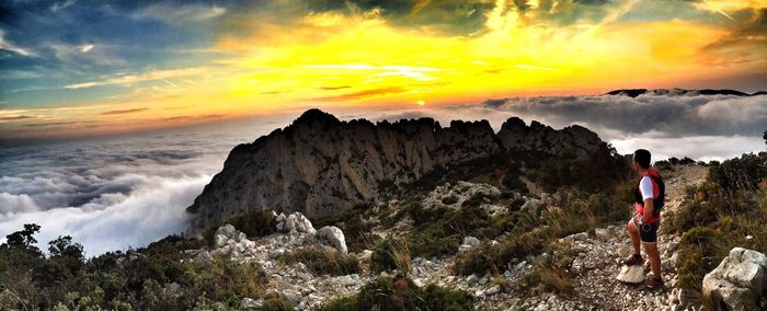 Man standing on cliff against sky during sunset