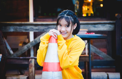 Portrait of smiling young woman holding traffic cone while standing at roadside