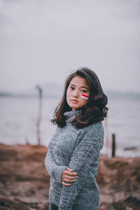 Beautiful young woman standing at lake against sky