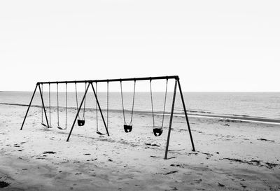 View of a empty unused set of swings on a empty beach against a cloudy sky early one morning