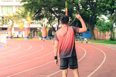 Rear view of mid adult man holding racket while standing on sports track