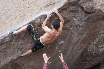 Rear view of shirtless man climbing on rock