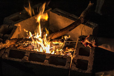 Cropped image of hand roasting marshmallows on campfire at night