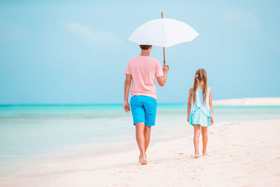 Rear view of father and daughter walking on beach