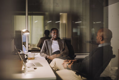 Smiling businesswoman planning strategy with male colleague seen through glass of work place