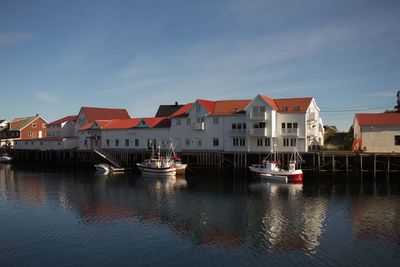 Boats moored on river by buildings against sky