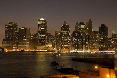 Illuminated buildings by river against sky at night