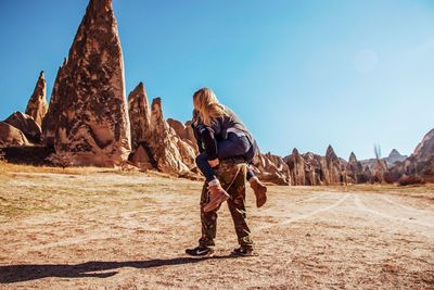 Full length of man giving piggyback to woman by rock formations against clear sky