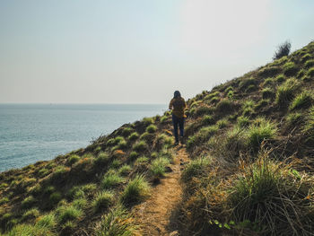 Rear view of man walking by sea against sky