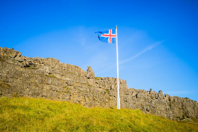 Low angle view of flag on mountain against blue sky