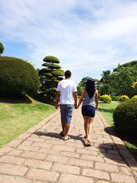 Rear view of couple holding hands while walking on footpath in park
