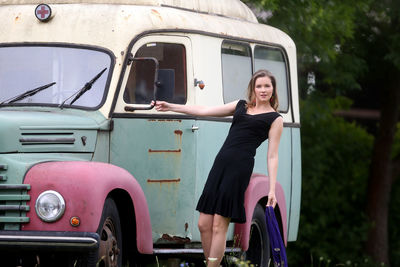 Portrait of woman standing by old van outdoors