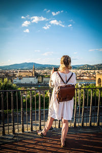 Rear view of woman standing by railing against sky