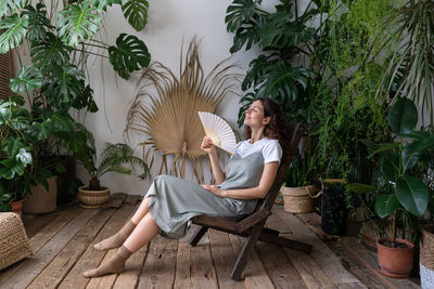 Happy woman florist refreshing in home garden breathing fresh air hold paper fan in hand at hot day