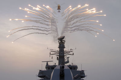 Low angle view of fireworks display over ship by helicopter in sky 
