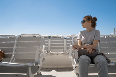 Young woman sitting on seat against clear sky