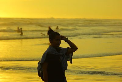 Silhouette woman standing at beach against sky during sunset