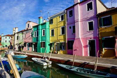 Boats moored in canal by buildings against sky